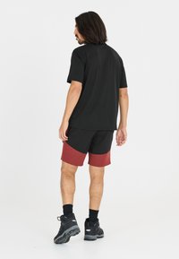 Svart kortärmad t-shirt i kombination med svart och vinröd färgblockerad shorts. Modellen har på sig svarta stövlar och mörka strumpor, stående bakifrån.