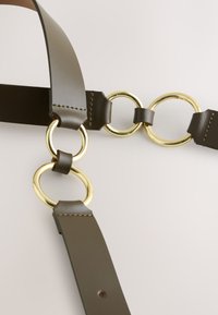 Brązowy skórzany pasek z metalowymi pierścieniami i ozdobami w kolorze złotym. Charakteryzuje się gładką teksturą, mocnym przeszyciem i regulowaną długością.