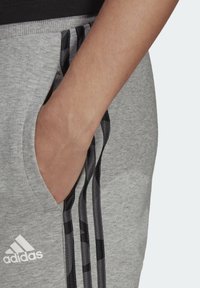 Grå sweatpants med svarta sidostråk, elastisk midjebands och sidofickor; logotyp i vitt framtill.