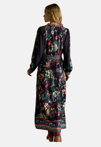 Pikk tumesinine kleit, millel on erksavärviline lilleline tikand, kogutud vöökoht, pikad varrukad ja mustriline äär. Sile kangastekstuur.