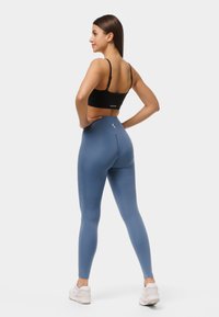 Melna īsā torte un augsto jostasvietu zilas legingas, kas izgatavotas no elastīga auduma; gluda tekstūra ar logotipa akcentu legingu aizmugurē.