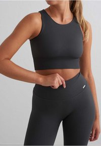 Pelēks ribots sporta tops un leggins ar teksturētu apdari. Topam ir apaļa kakla izgriezums, bet leggingiem ir augsts jostasvietas dizains.