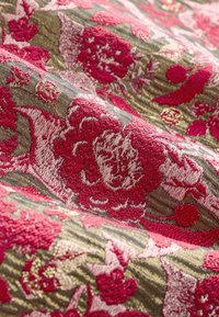Textil mit einem kunstvollen Blumenmuster in Rosa und Rot auf einem strukturierten grünen Hintergrund, das ein reiches, gewebtes Design zeigt.