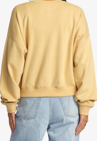 Sudadera amarilla de gran tamaño con escote redondo, puños y dobladillo acanalados. Tejido suave y texturizado, vista desde la parte de atrás, con un corte holgado.