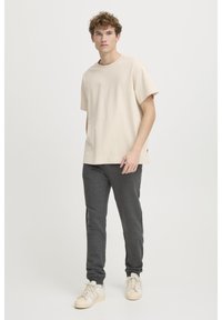 Cremefarvet t-shirt med korte ærmer kombinert med mørkegrå tapered bukser, der har en afslappet pasform og blød stof, kompletteret med lyse sneakers.