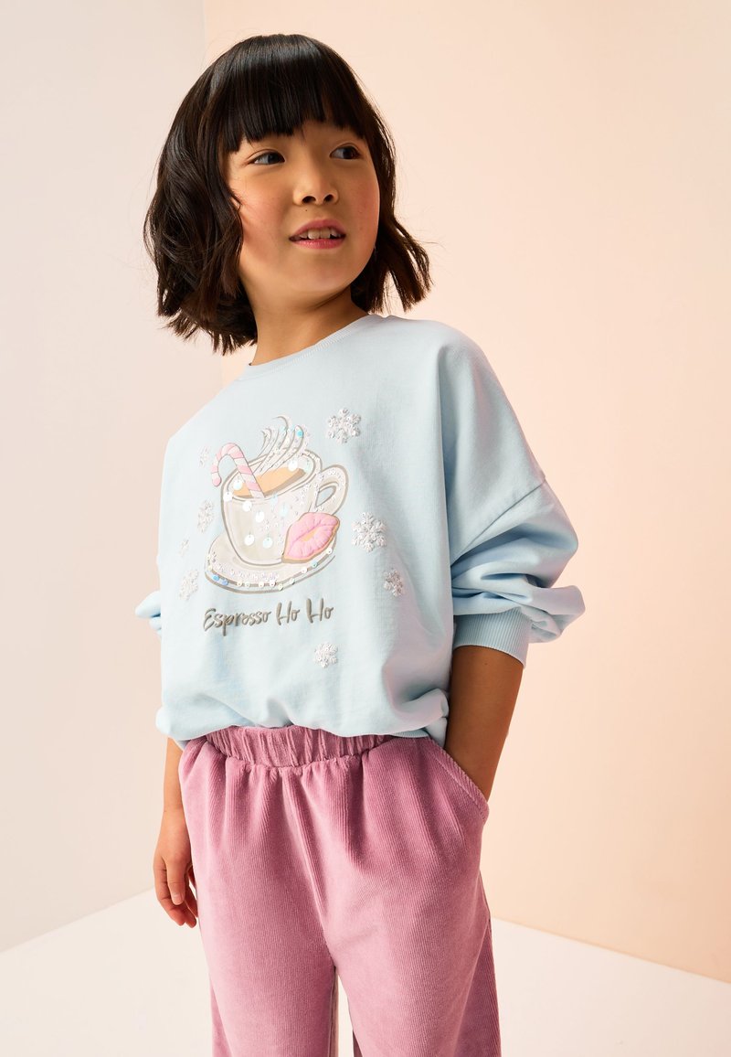 Sweat-shirt bleu clair avec un motif de tasse de café, un sucre d'orge et des lèvres. Associé à un pantalon en velours côtelé rose avec une taille élastique.