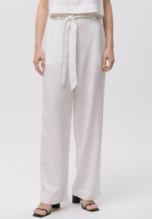 Pantaloni bianchi a vita alta con cintura annodata, gambe larghe, tessuto leggero e superficie liscia. Abbinati a sandali neri con tacco a blocco.