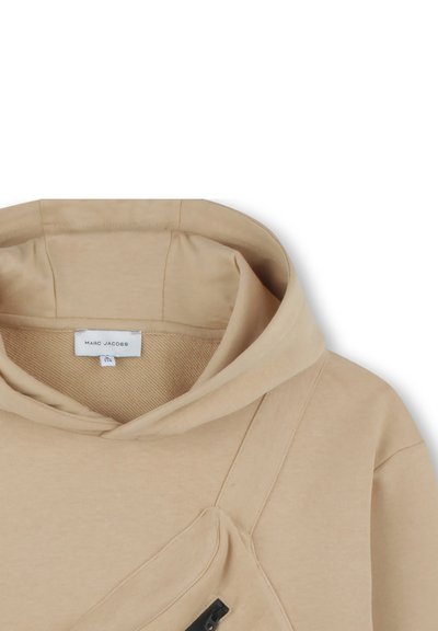 Hoodie beige en tissu doux avec une grande capuche, poche zippée noire à l'avant et une étiquette "Marc Jacobs" à l'intérieur.