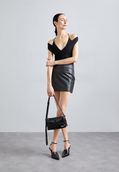 Čierny top s odhalenými ramenami, skombinovaný s čiernou koženou mini sukňou. Doplnky zahŕňajú čiernu crossbody tašku a špicaté podpätky.