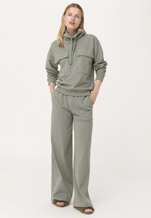 Conjunto de loungewear verde claro que incluye un sudadera de cuello alto con dos bolsillos delanteros y pantalones de pierna ancha fabricados en un tejido suave.
