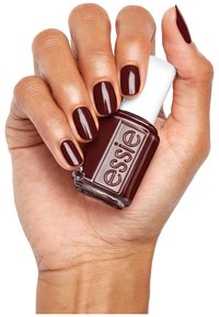 Smalto per unghie di un oscuro color borgogna in una bottiglia di vetro con un tappo bianco, tenuto in una mano che mostra unghie curate verniciate dello stesso colore.