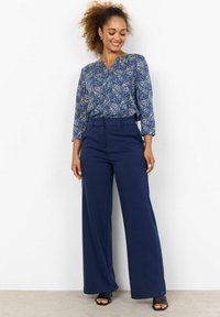 Blue paisley-patterned blouse with three-quarter sleeves, paired with navy wide-leg trousers. Smooth fabric and relaxed fit, worn with black heeled sandals.