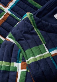 Pikowana tkanina w granatowym kolorze z geometrycznym wzorem zielonych, białych, brązowych i turkusowych pasków. Gładka tekstura z widocznym przeszyciem.