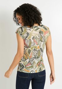 Top ajustado de manga corta en tejido ligero con un patrón de hojas multicolores, que presenta tonos de verde, rosa y beige con contornos negros.