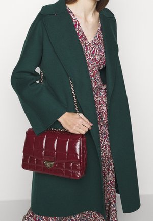 Manteau en laine vert, robe à motif floral, et sac à main matelassé bordeaux avec une bandoulière chaîne et des détails métalliques.