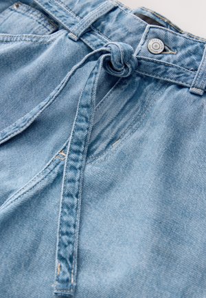 Šviesiai mėlyni džinsiniai šortai, kuriuose yra susirišimas mazgu juosmens srityje, subtilus išblukimas ir sagų užsegimas. Audinys minkštas, su matomomis siūlėmis.