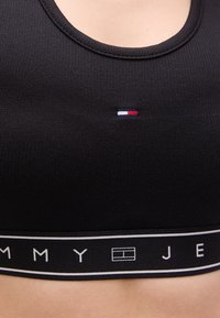 Μαύρο αθλητικό σουτιέν με ριμπ ύφανση, στρογγυλή λαιμόκοψη, μικρό κεντημένο τρικολόρ λογότυπο και λάστιχο με λευκές λεπτομέρειες και λογότυπο.