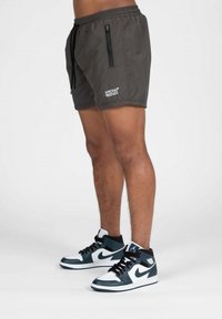 Grijze zwemshorts met een elastische tailleband en trekkoord, voorzien van een ritszak en een wit logo. Gepaard met zwart-witte sneakers.