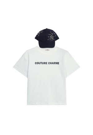 Witte katoenen T-shirt met de tekst "COUTURE CHARME" in marineblauw. Gecombineerd met een marineblauw pet versierd met kleurrijke versieringen.