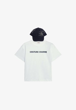 Camiseta de algodón blanca con el texto "COUTURE CHARME" en color marino. Combinada con una gorra marina adornada con coloridos embellishments.