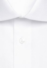 Gros plan d'un col de chemise blanche et d'un seul bouton blanc sur la patte de boutonnage avant.