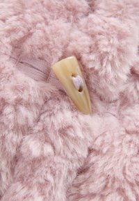 Tessuto rosa peloso con una texture morbida, caratterizzato da un bottone color avorio con un foro centrale per la chiusura.