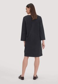 Dunkelgraues, knielanges Kleid mit langen Ärmeln, runder Ausschnitt und minimalistischem Design. Glatter Stoff mit gerader Silhouette.