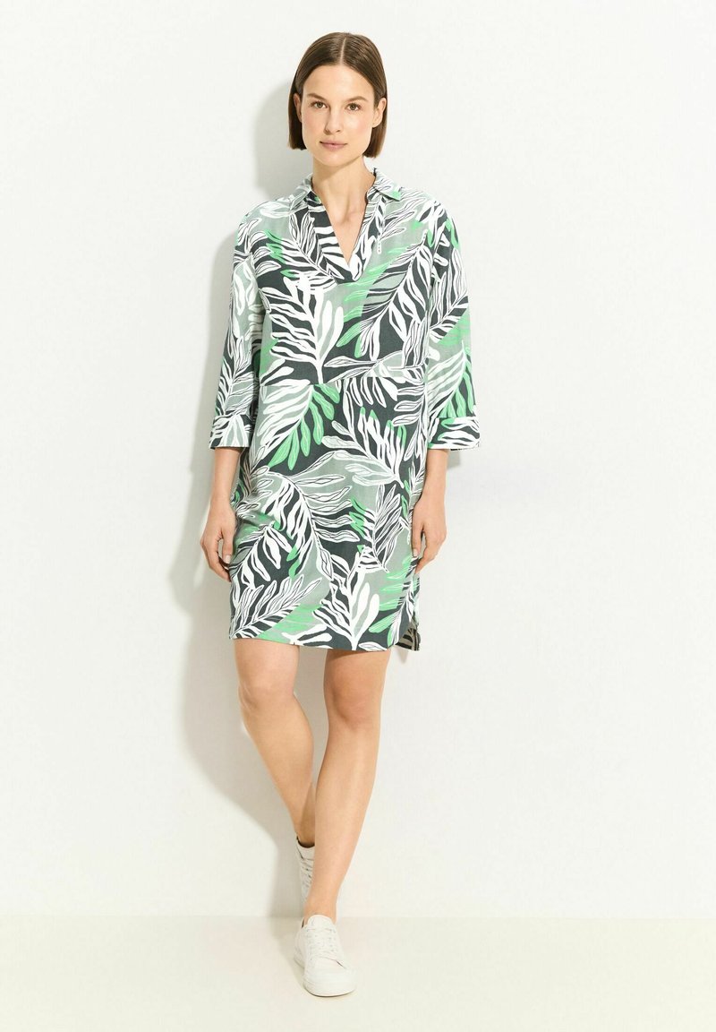 Floral-patterned dress with green, white, and black leaves. Lightweight fabric, collar design, three-quarter sleeves, and side slits.