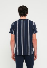 Μπλε ναυτικού χρώματος κοντομάνικη μπλούζα με κάθετες λευκές και μπλε ρίγες· στρογγυλή λαιμόκοψη· απαλό ύφασμα· άνετη εφαρμογή· διακριτή υφή.