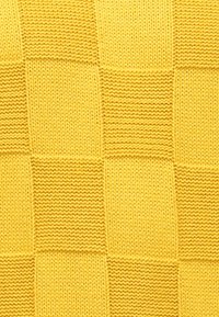 Žltá pletená látka s kockovaným vzorom, ktorý obsahuje striedavé textúrované štvorce a hladké časti, vytvárajúc vizuálny kontrast.