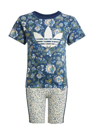 Kurzärmliges Hemd in Marineblau mit floralem Muster und weißem Logo, kombiniert mit engeren floralen Shorts in Creme mit blauen Akzenten und seitlichen Streifen.