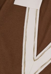 Tessuto marrone con un pannello bianco accentuato e dettagli di cucitura. Superficie strutturata con schemi e combinazioni di colori contrastanti.