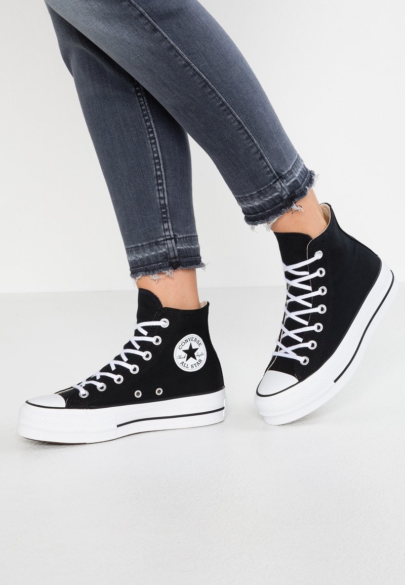 Černé vysoké plátěné tenisky s bílými tkaničkami a gumovými podrážkami, s kruhovým logem "Converse All Star" na vnější straně.