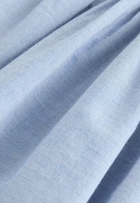 Helles blaues Gewebe mit glatter Textur, das subtile Falten und ein feines, atmungsaktives Webmuster aufweist. Geeignet für verschiedene textile Anwendungen.