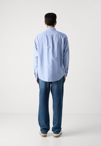 Blau-weiß gestreifte Button-Down-Bluse mit lockerer Passform, kombiniert mit lockeren blauen Jeans. Das Hemd verfügt über einen klassischen Kragen und eine Rückennaht.