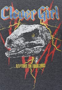 T-shirt grafico con testa di dinosauro e testo "Clever Girl" in blu. Tessuto grigio con accenti di fulmini rossi e gialli e dettagli del tour.