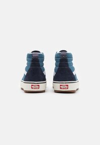 Høye sneakers med blå og marineblå semsket skinnpaneler, hvite detaljer, gummisåler og en rød Vans-logo på hælen.
