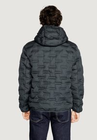 Giubbotto puffer grigio scuro con cappuccio, caratterizzato da sezioni trapuntate e una superficie liscia e lucida. Indossato sopra jeans scuri.