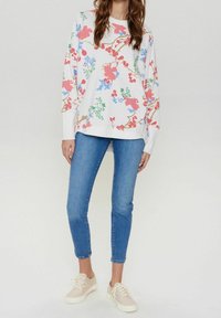 Vitt tröja med färgglad blommönster i rosa, blått och grönt, ihop med åtsittande blå jeans och ljusa sneakers.