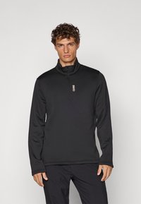 Sudadera con cremallera negra y cuello alto, elaborada en tejido suave, con un logo sutil en el pecho y una textura suave.