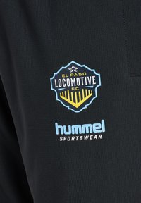 El Paso Locomotive FC-logo over lyseblåt "hummel sportswear" tekst på sort tekstureret stof, sandsynligvis sportstøj.