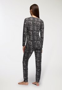 Completo pigiama a maniche lunghe, aderente, grigio con stampa leopardata nera. Tessuto morbido, texture liscia e gambe affusolate. Nessun hardware o decorazione visibile.