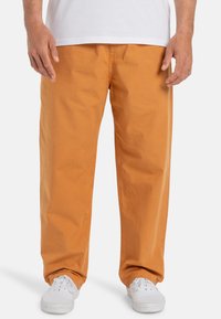 Orange, loose-fitting cotton pants with a smooth texture, featuring side pockets and a waistband visible at the top. Worn with white sneakers.