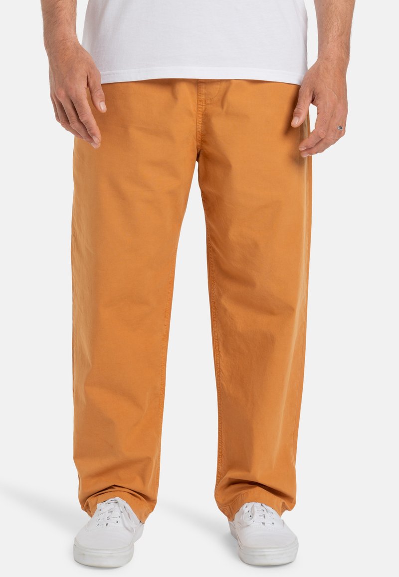 Orange, loose-fitting cotton pants with a smooth texture, featuring side pockets and a waistband visible at the top. Worn with white sneakers.