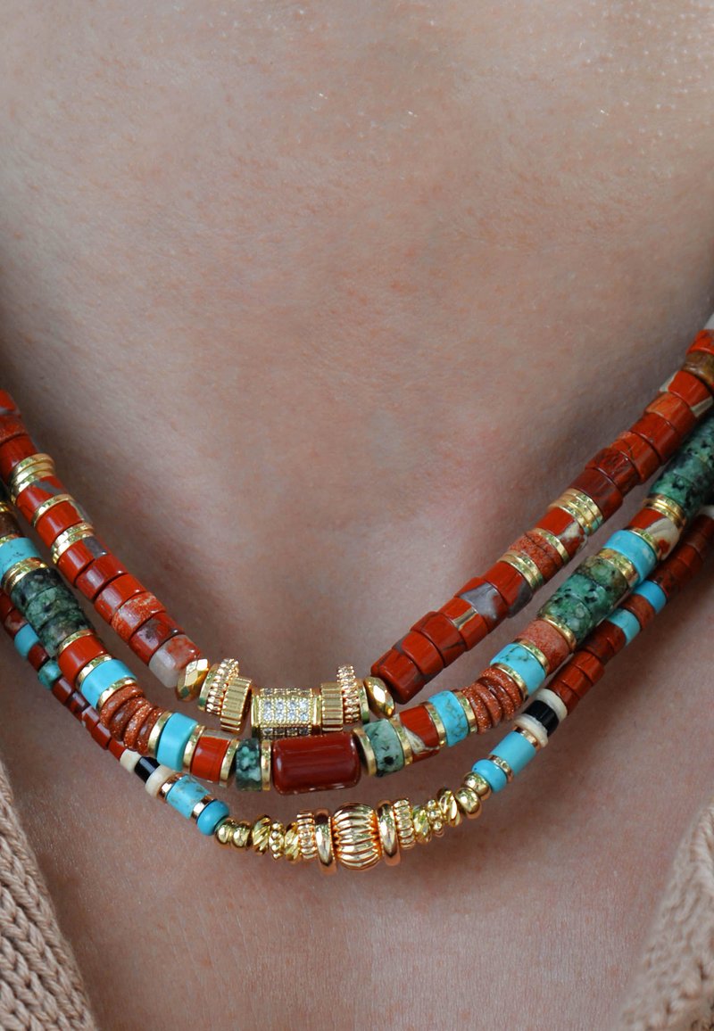 Collier en perles multicolores featuring des pierres rouges, turquoises et vertes avec des accents dorés, disposées en couches avec des motifs géométriques.