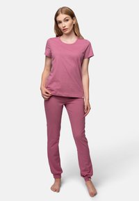 T-shirt in cotone rosa con maniche corte e scollo rotondo, abbinato a pantaloni rosa coordinati con polsini elastici e una piccola etichetta con logo.