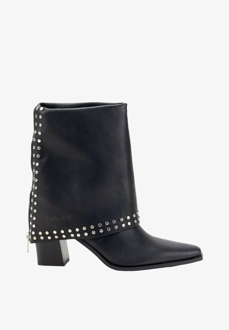 Botín negro al tobillo con punta afilada, confeccionado en material suave. Presenta tachuelas plateadas a lo largo de la parte superior y un tacón grueso tipo bloque.