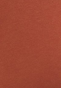 Tecido de suéter tricotado em uma rica cor terracota, apresentando uma textura suave com padrões de nervuras finas e consistentes por toda a parte.