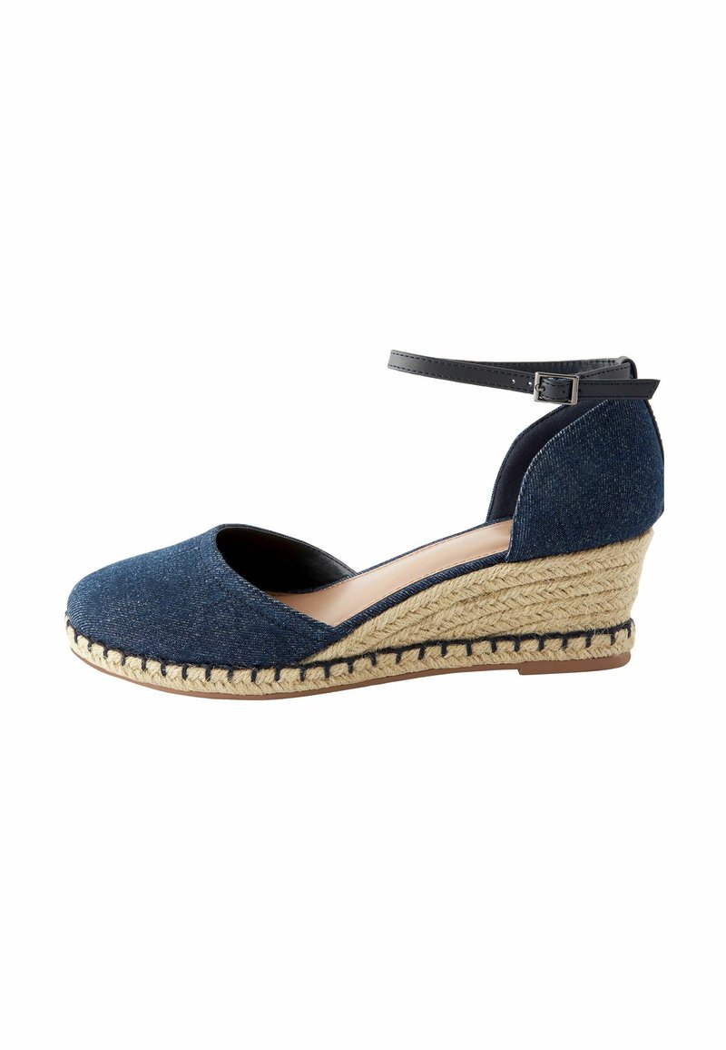 Espadrille compensée bleu marine avec talon en jute tressé, bout fermé, et bride de cheville noire avec boucle.