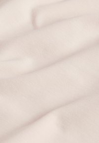 Tela suave de color beige pálido con textura fina acanalada y pliegues suaves que crean sombras sutiles.